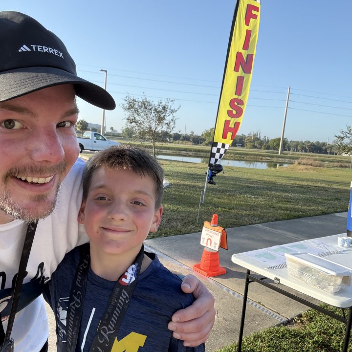 US Road Running race day photo with runners, walkers, finisher medals, and race staff